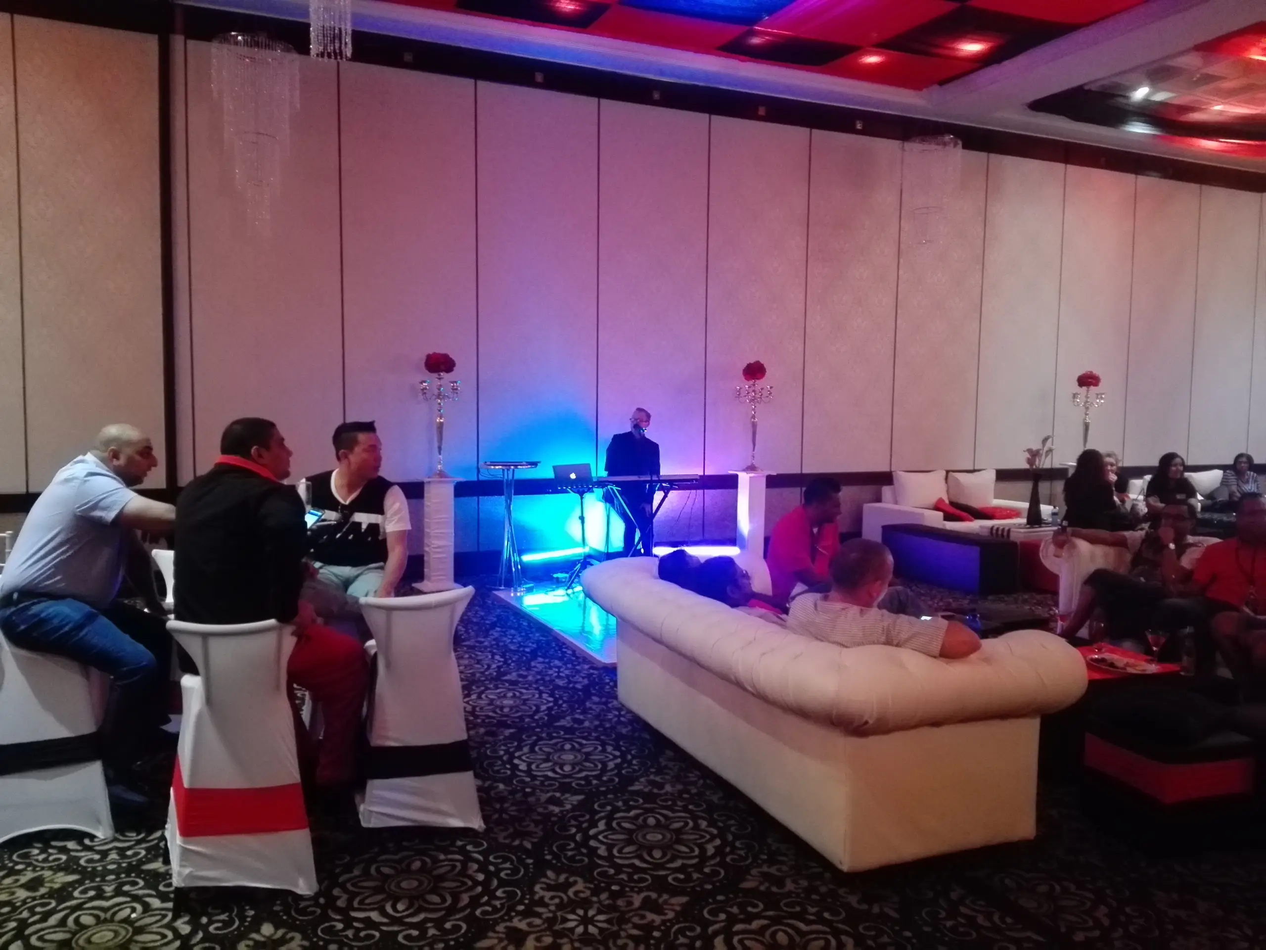 Guests on white couches and high chairs in a lounge with pink and blue uplighting