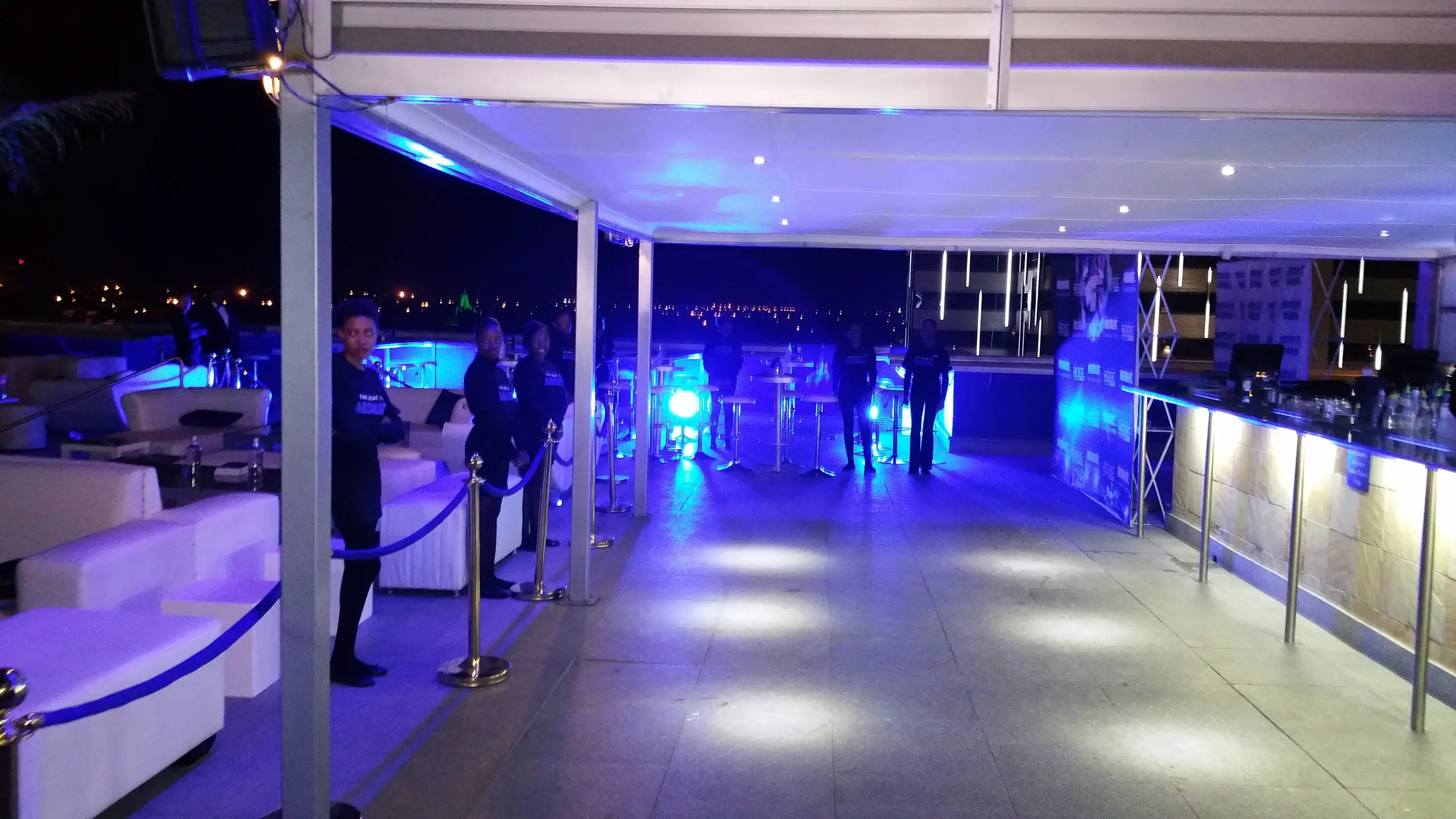A marquee at night with a lit bar, lounge furniture and blue uplighting
