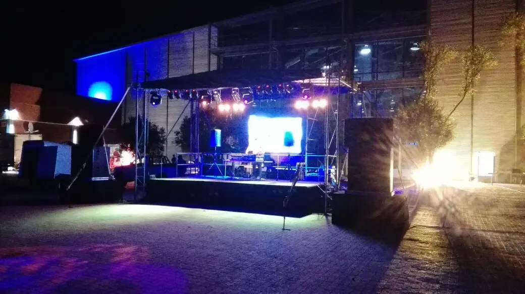 An outdoor stage at night with an LED screen, lighting and a band setting up