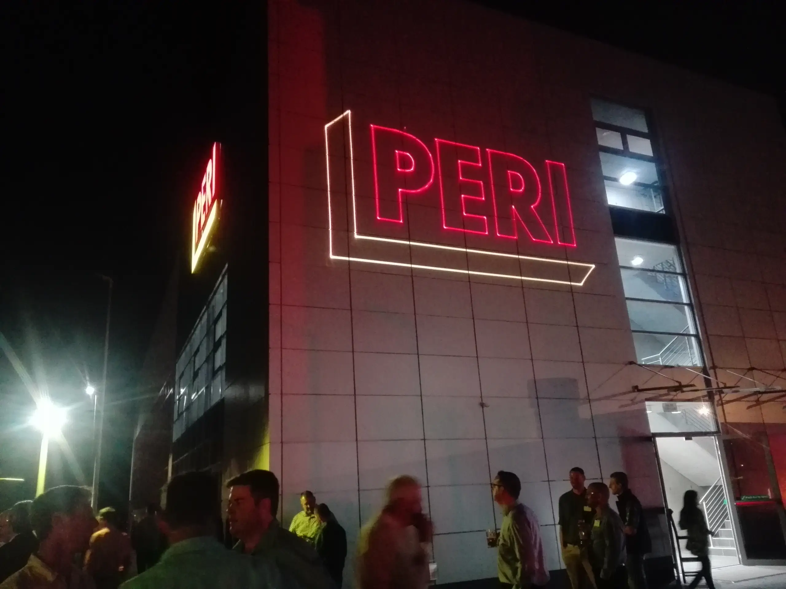 The PERI building at night with a red laser outline drawn around its sign, guests outside