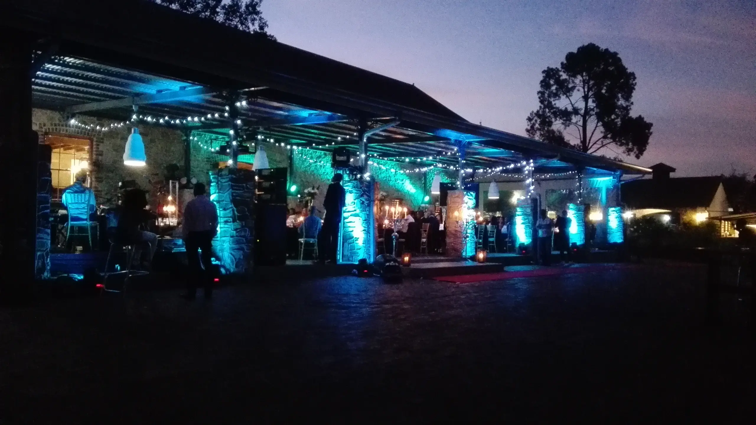 A venue's veranda uplit in cyan at dusk, with tables set under it