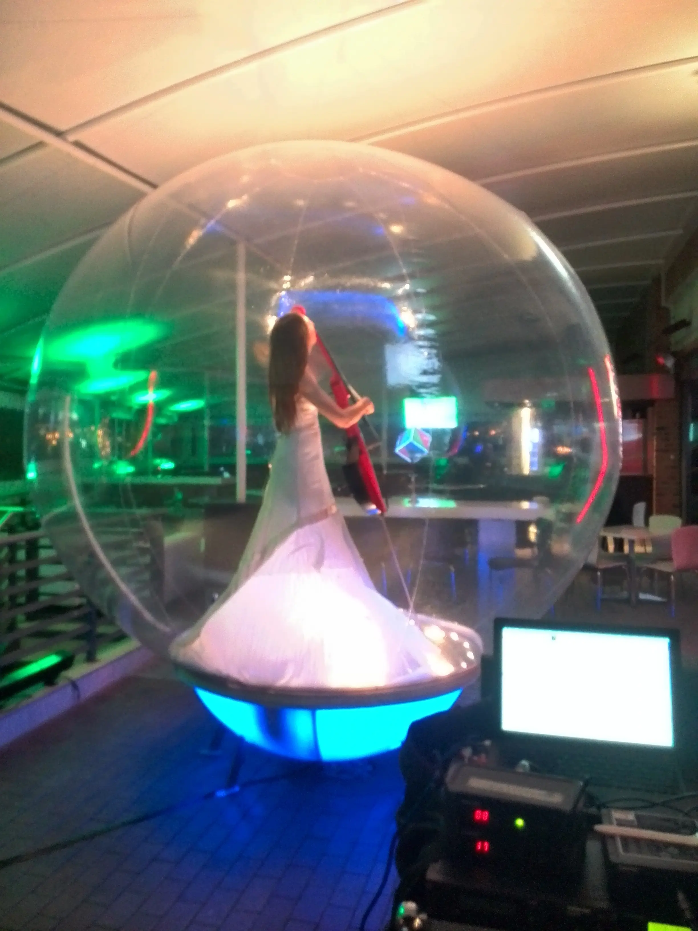A performer in a white gown inside a clear bubble lit from below in green
