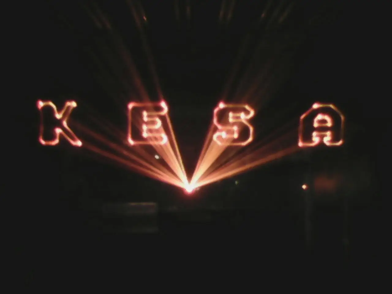 KESA written in red laser light above a fan of beams, at night