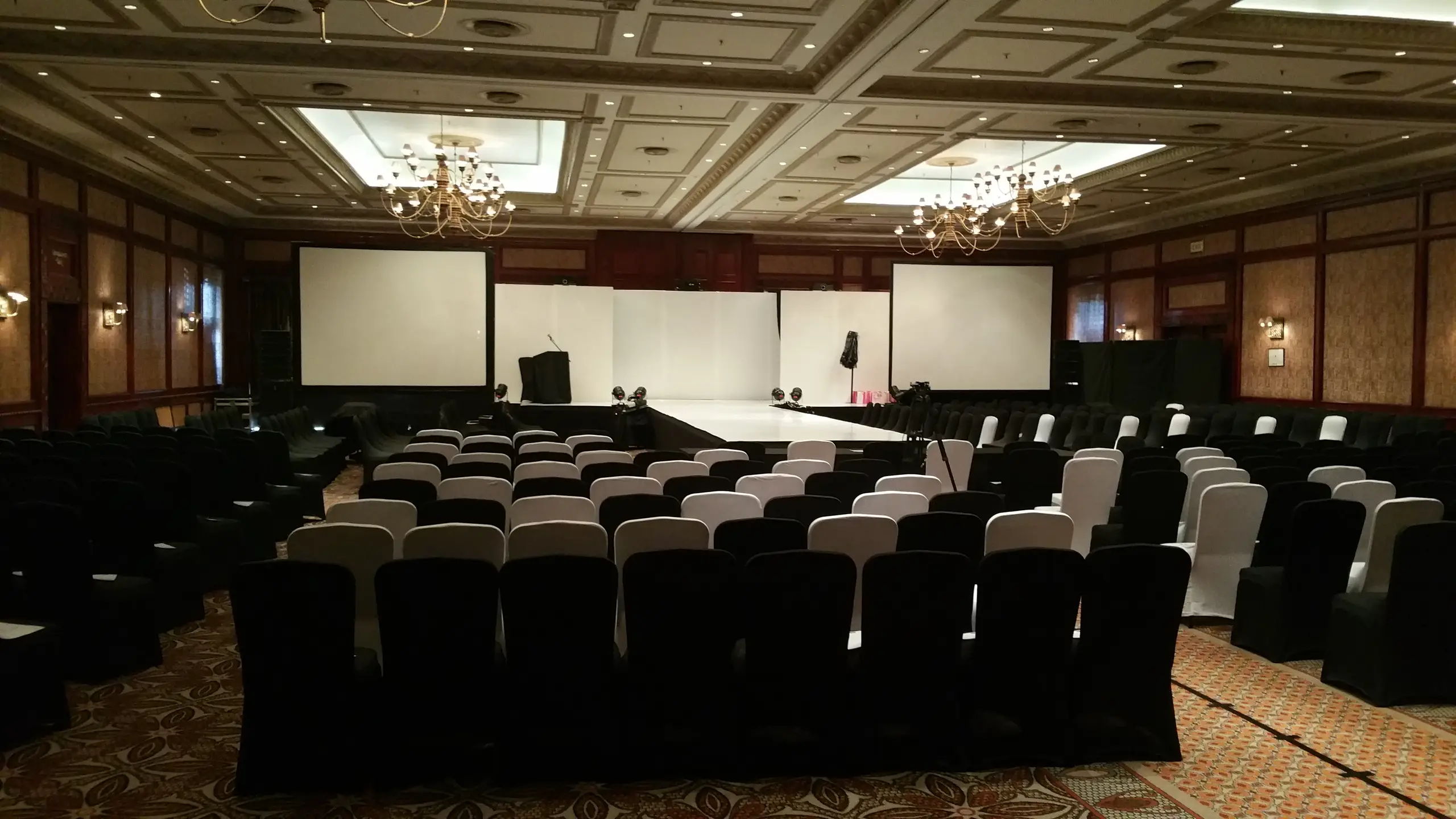 A conference hall with rows of covered chairs facing a stage between two projection screens